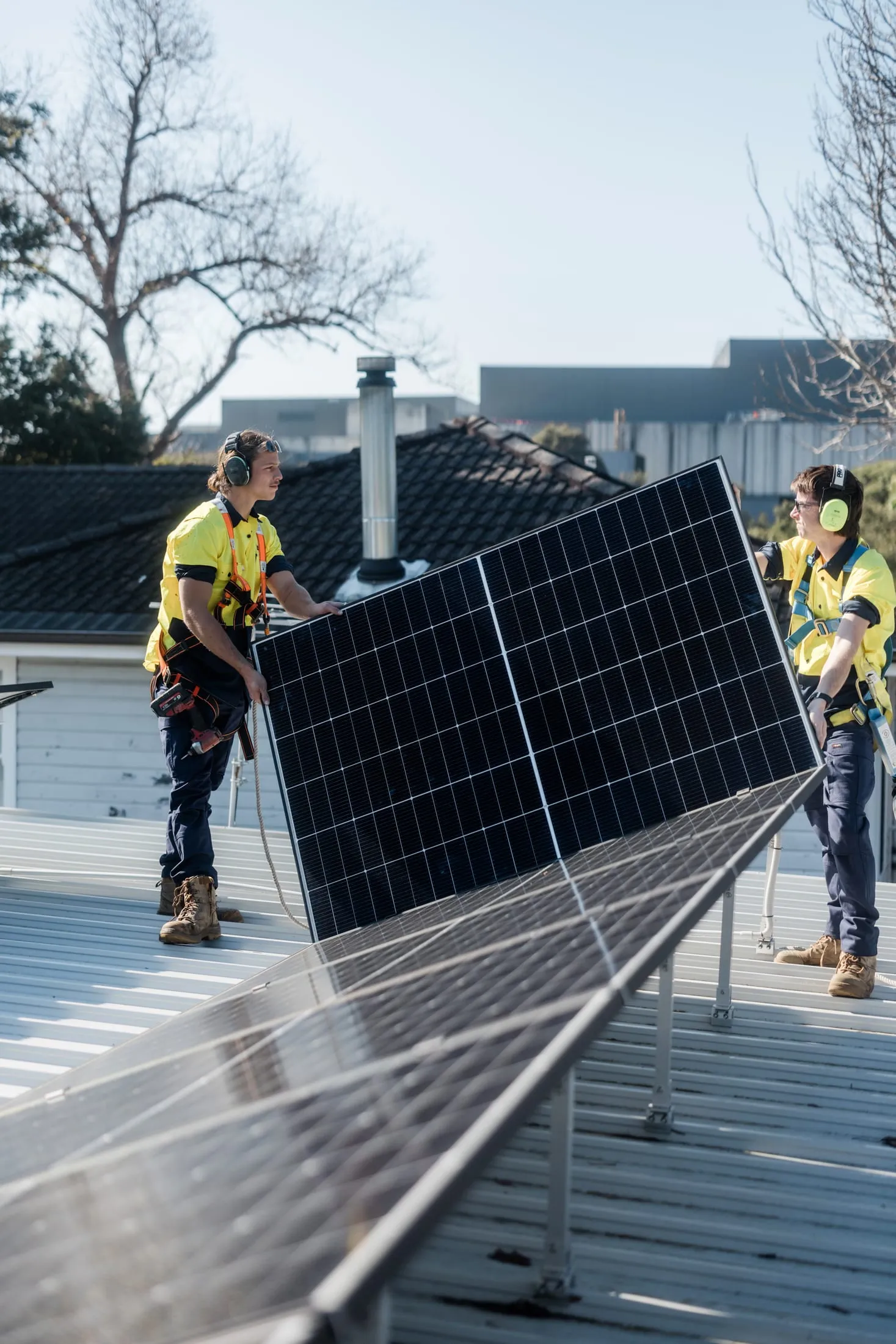 Electrified Industries installers positioning a solar panel on a Newcastle roof